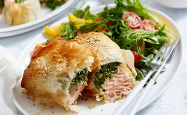 Baked salmon and spinach feta parcel with mixed greens on a white plate.