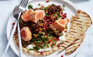 Seared salmon with almond salad, labne, pomegranate, diced vegetables, and grilled flatbread on a white plate.