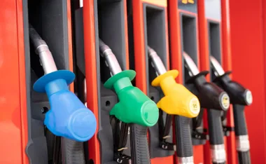 Colorful fuel pump nozzles at a petrol station, including blue, green, yellow, and black.