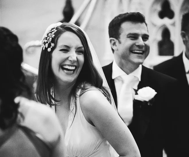A bride and groom laughing joyfully during their wedding ceremony, captured in a black and white photo.