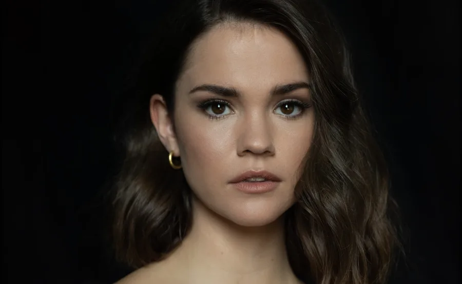 A person with shoulder-length brown hair and hoop earrings against a dark background.