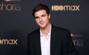 Man in a black suit and white shirt at HBO Max's "Euphoria" event, standing in front of a branded backdrop.