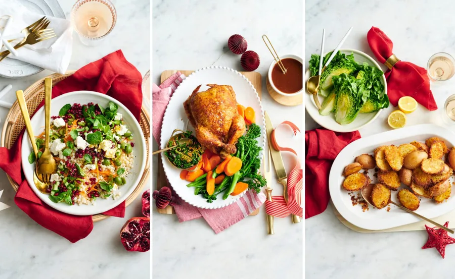 Festive holiday meal with salad, roasted chicken with vegetables, and crispy potatoes on a marble table.