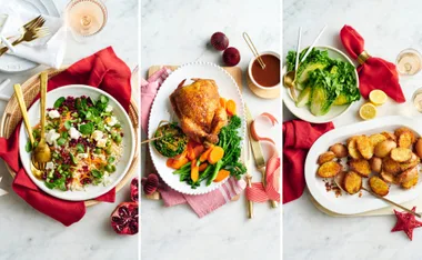 Festive holiday meal with salad, roasted chicken with vegetables, and crispy potatoes on a marble table.