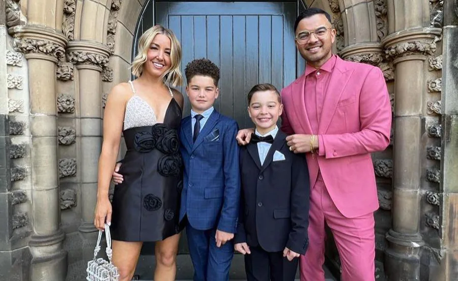 Family of four smiling, dressed formally in suits and a dress, standing in front of an ornate building entrance.