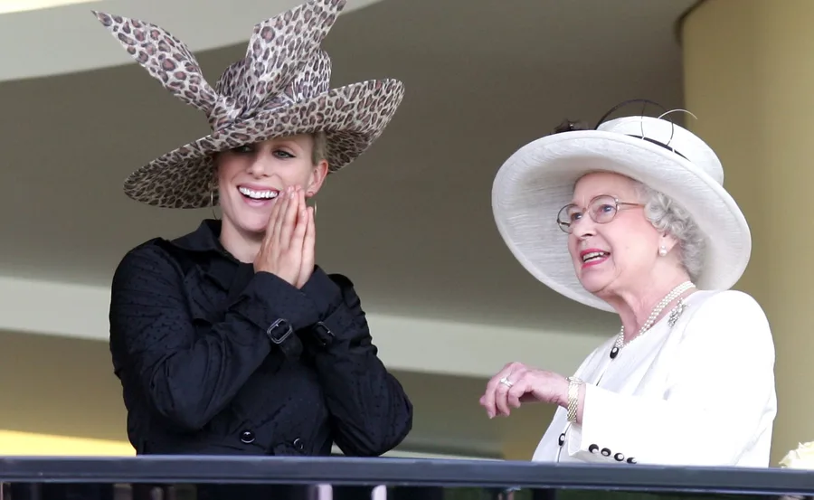 Two women wearing stylish hats smile and converse, one in leopard print and one in white.