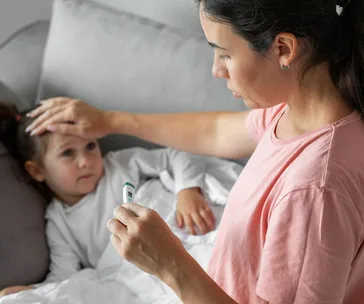 A woman checks a sick child's temperature with a digital thermometer, while feeling her forehead.