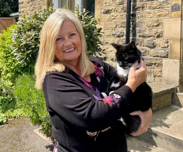 A woman smiling outside a stone building, holding a black and white cat.