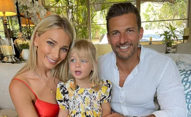Family of three smiling on a couch, with indoor plants in the background.
