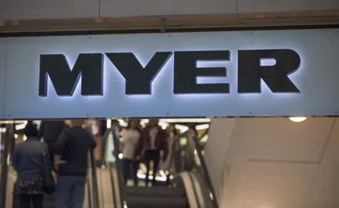 Sign for Myer department store above a busy escalator with shoppers.