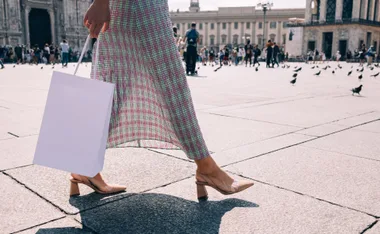 Person walking with shopping bag and wearing beige heels on a city square.
