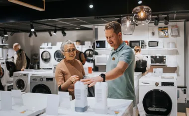Salesperson assisting a customer while shopping for appliances in a store, surrounded by washing machines.
