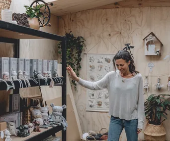 A woman in a cozy room surrounded by handmade toys and plants, creating a calming atmosphere for kids.