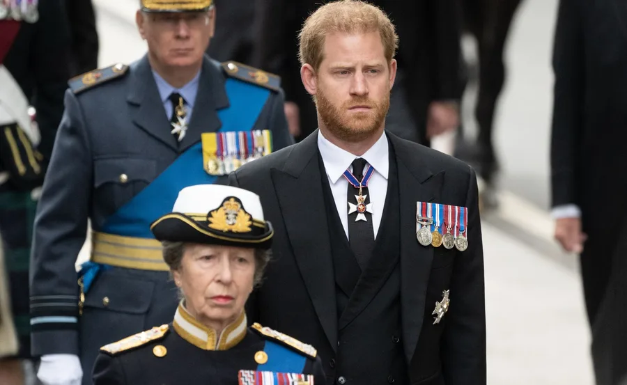 Royal procession with a woman in uniform and a man in a suit, both wearing medals, walking in a formal event.