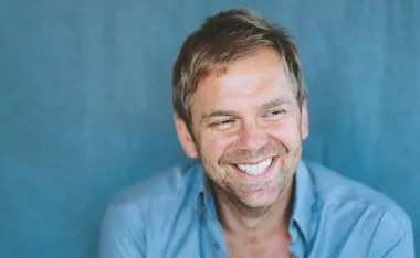 Smiling man in a light blue shirt against a blue background.