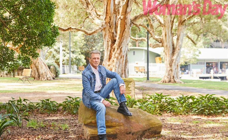 Man in denim outfit sitting on a rock in a park with trees, appearing in Woman's Day magazine.