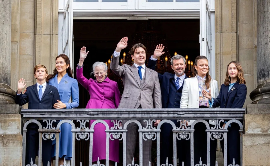 Danish royal family waving from a balcony during a public appearance, smiling and dressed formally.