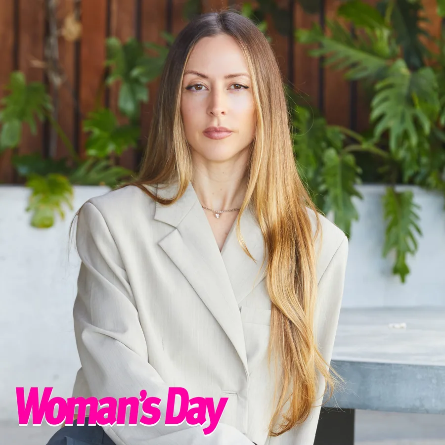 Woman with long hair in a beige blazer sitting, plants in the background, Woman's Day logo in the corner.