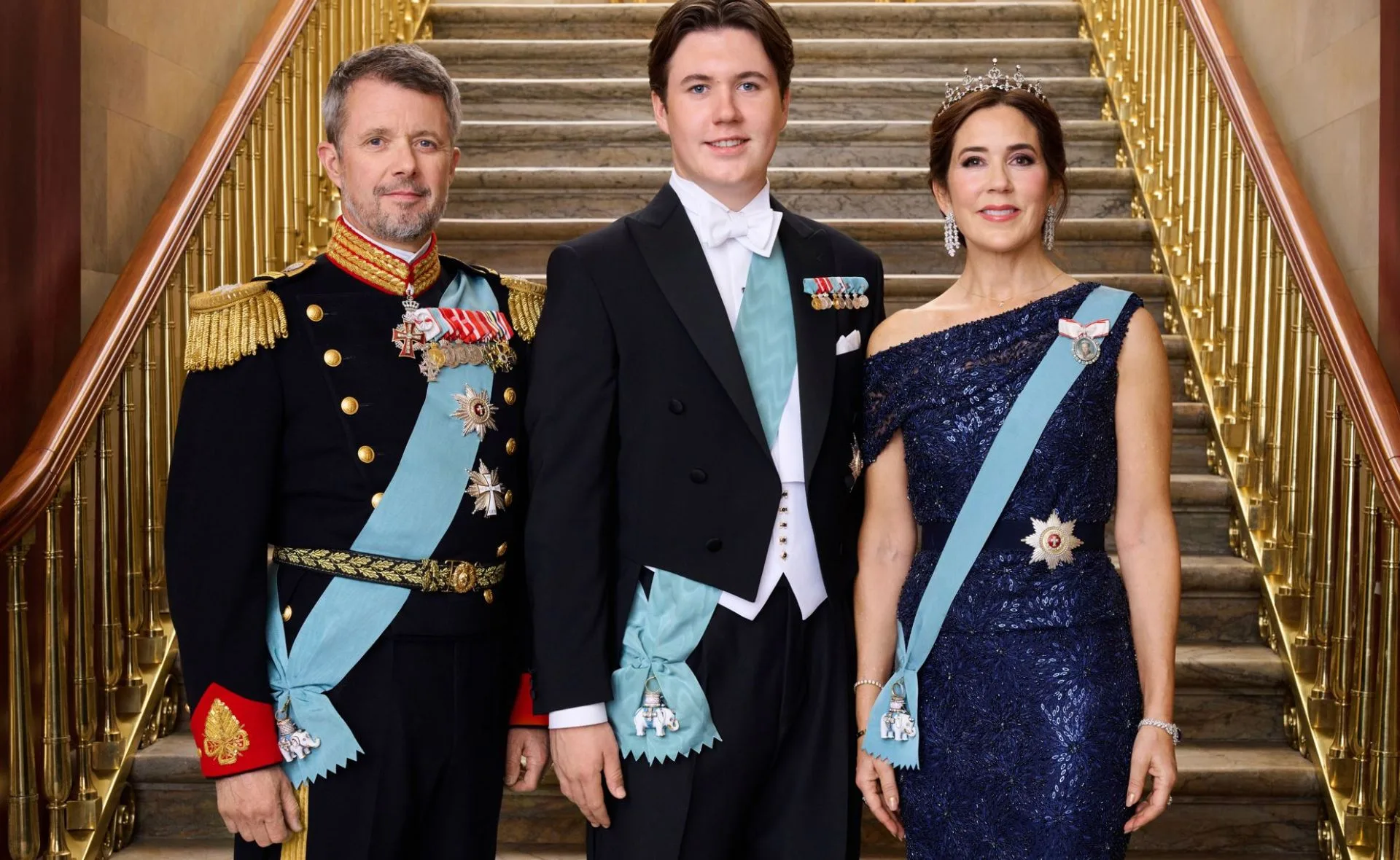 A family in formal attire poses on a grand staircase, wearing ceremonial sashes and medals.