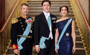 A family in formal attire poses on a grand staircase, wearing ceremonial sashes and medals.