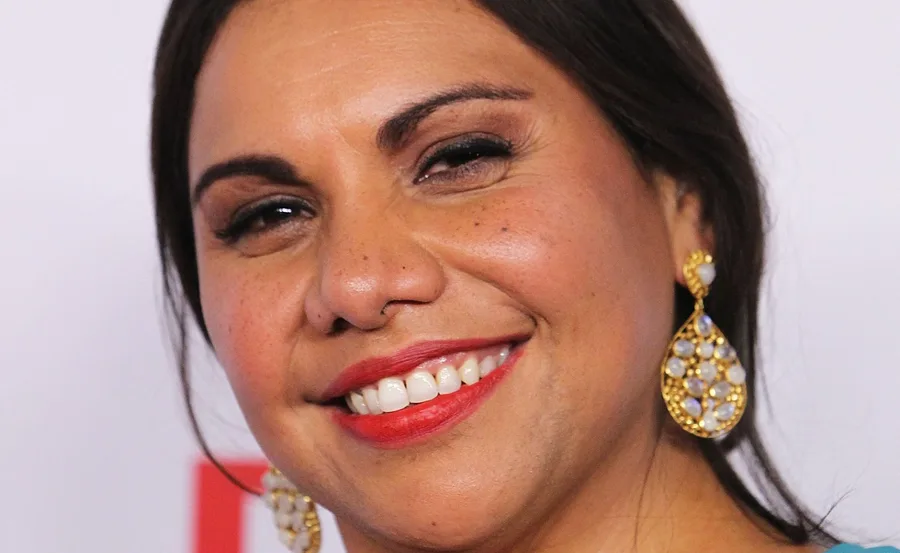 Smiling woman with long hair, gold earrings, and red lipstick.