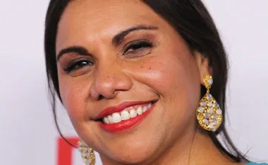 Smiling woman with long hair, gold earrings, and red lipstick.