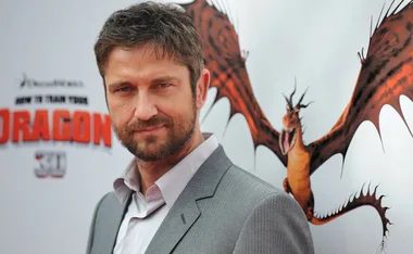 Man in gray suit at "How to Train Your Dragon" event with backdrop of flying dragon.