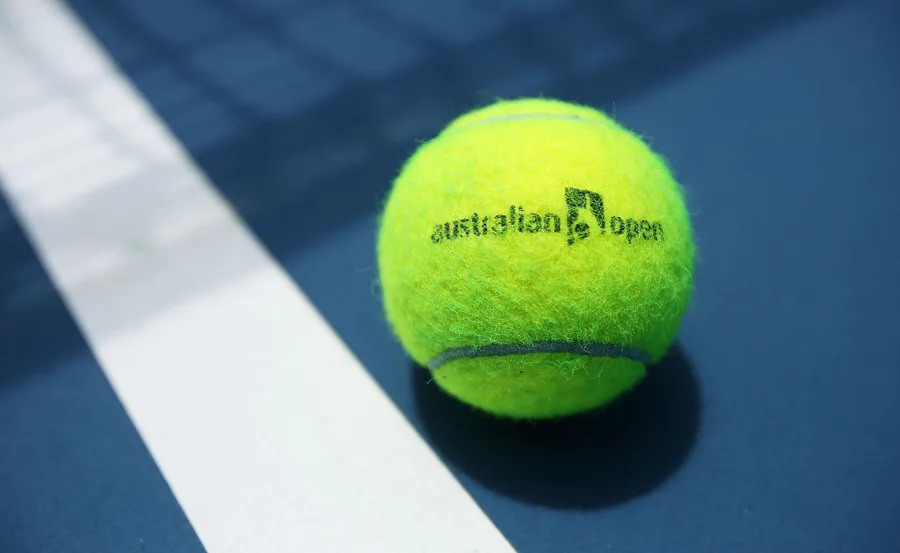 Tennis ball with "Australian Open" logo on a blue court near a white line.