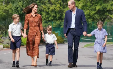 A family walking together outdoors, smiling, holding hands. Young children in school uniforms.