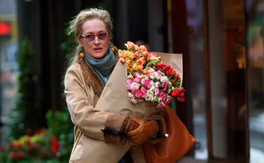 A person wearing sunglasses and a winter coat holds a bouquet of colorful flowers.
