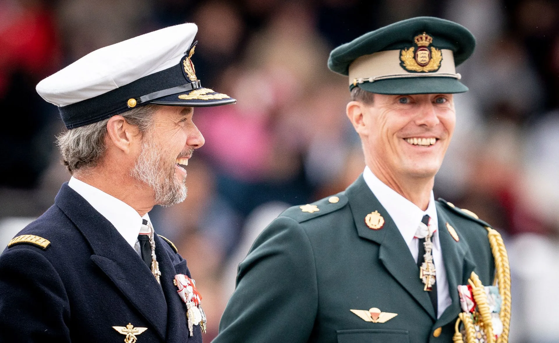 Two men in military uniforms smile during a formal event.