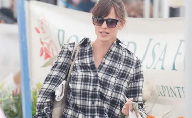 Person wearing sunglasses and a plaid shirt holding cash at an outdoor market.