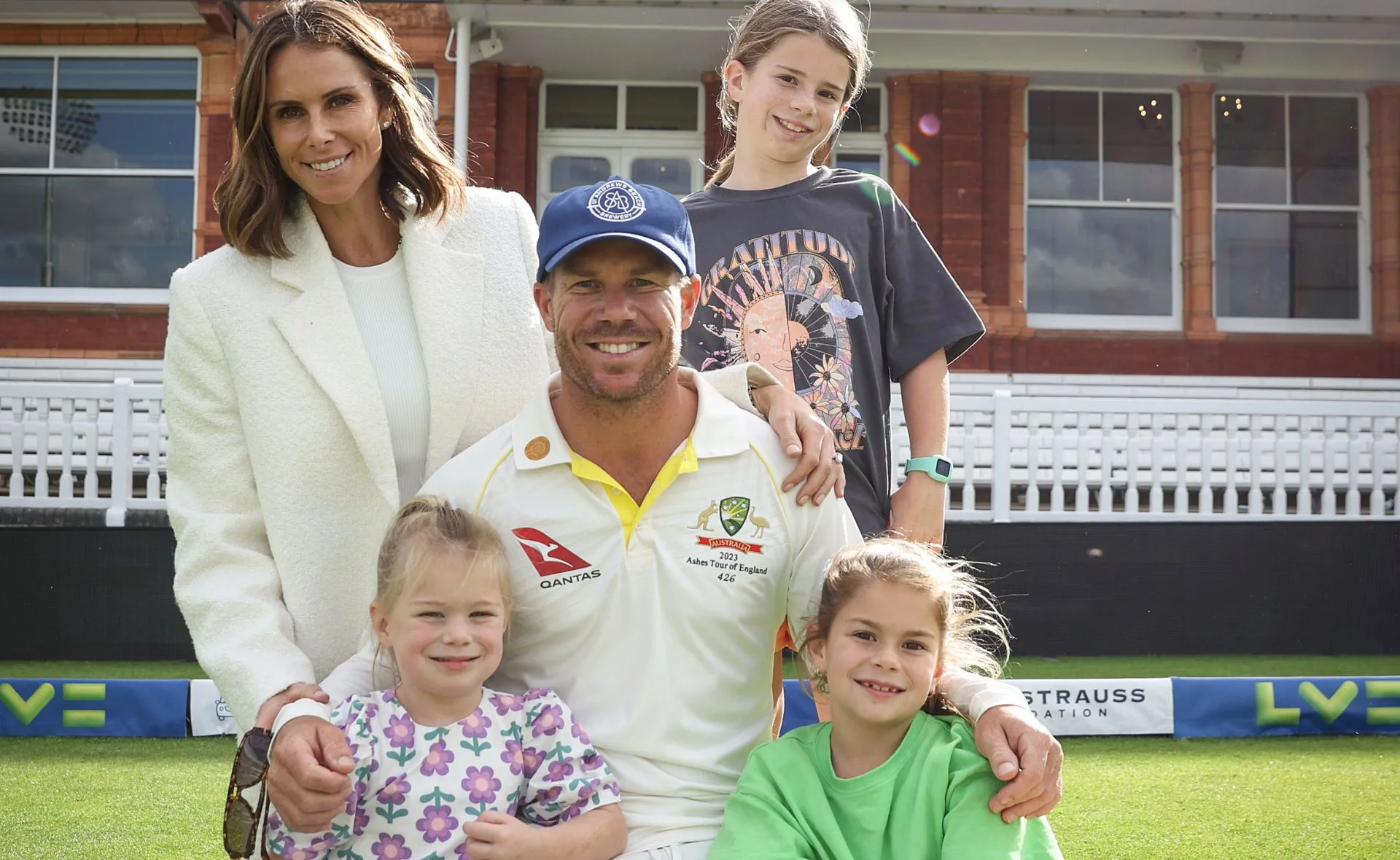 A man in a cricket uniform with a woman and three children in a sports field.