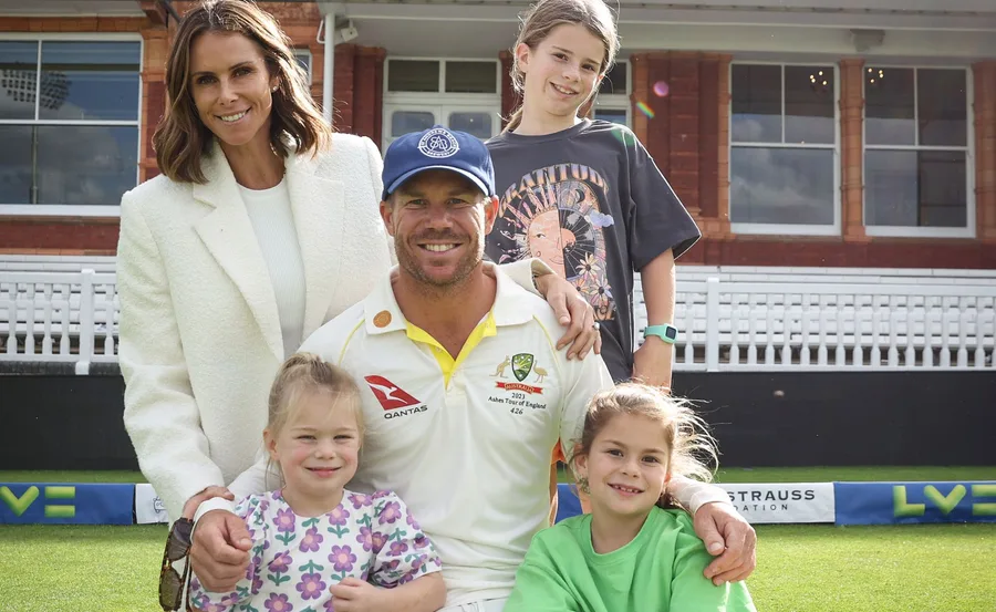 A man in a cricket uniform with a woman and three children in a sports field.