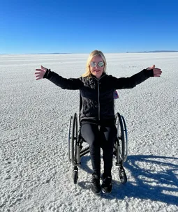 Person in a wheelchair with outstretched arms on a vast salt flat under a clear blue sky.