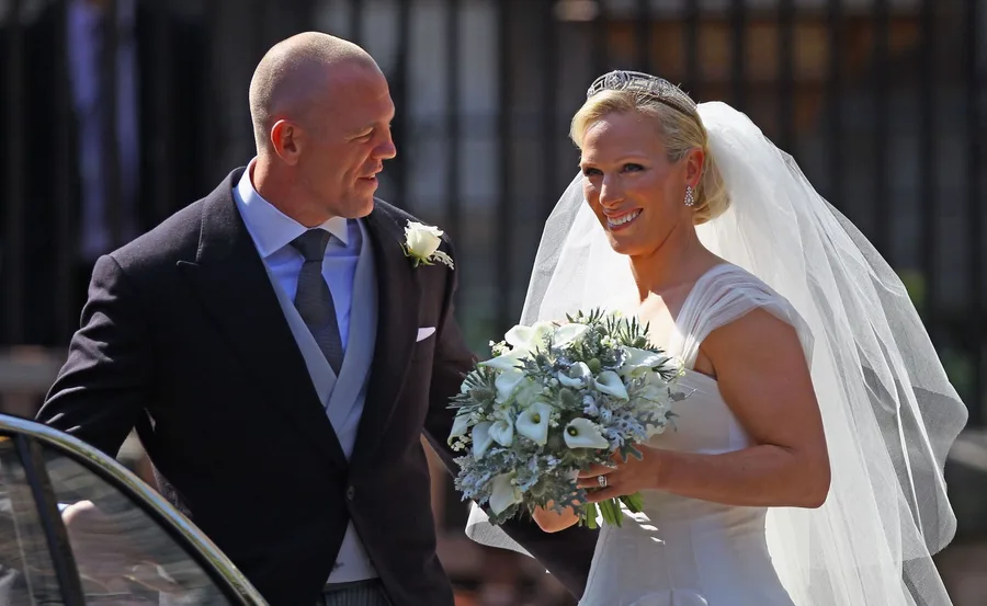 A bride and groom smiling at each other, with the bride holding a floral bouquet.