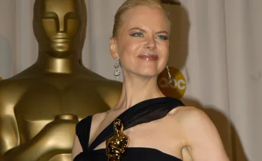 Oscar-winning actress holding her award, posing proudly on stage in an elegant black gown.