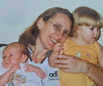 A smiling woman holds a baby and a young child in her arms, capturing a warm family moment.