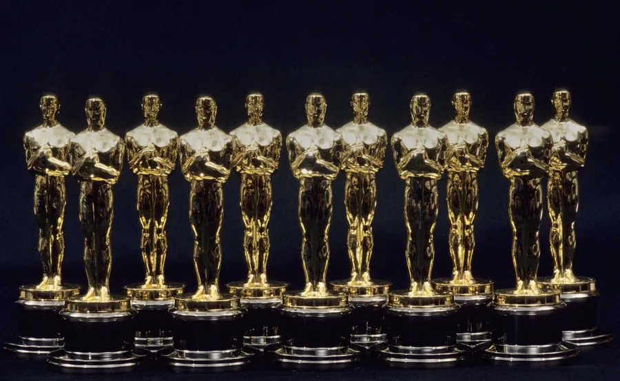 A row of nine golden Oscar statuettes on a black background.