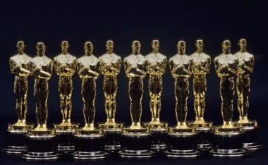 A row of nine golden Oscar statuettes on a black background.