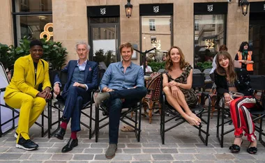 A group of five people sit on chairs outside Café 52, dressed in colorful and patterned outfits.