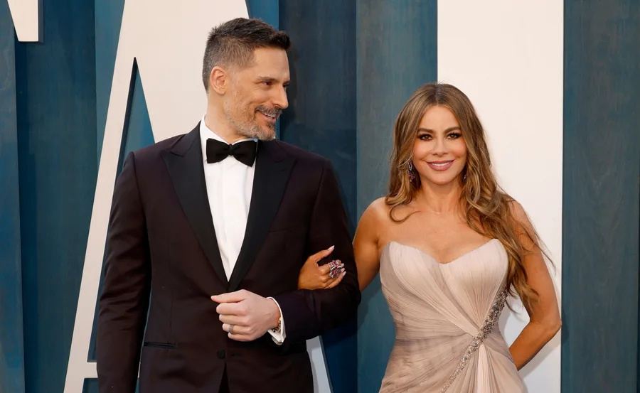 A couple in formal attire smiling, the woman wearing a strapless dress and the man in a tuxedo with a bow tie.
