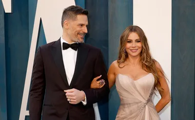 A couple in formal attire smiling, the woman wearing a strapless dress and the man in a tuxedo with a bow tie.