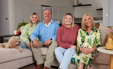 Family of four smiling on a couch with a dog in a cozy living room setting.