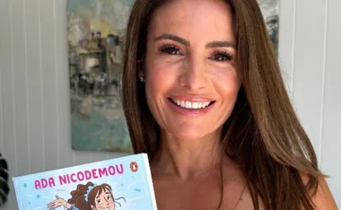 Smiling person holding a book titled "Ada Nicodemou" with a cartoon illustration on the cover.