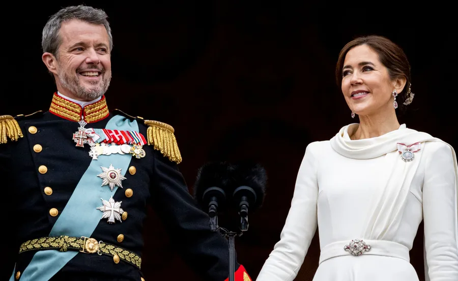 Royal couple in formal attire smiling and holding hands during a public appearance.