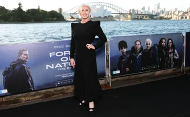 A woman in a black dress stands by a promotional poster for "Force of Nature" near Sydney Opera House.