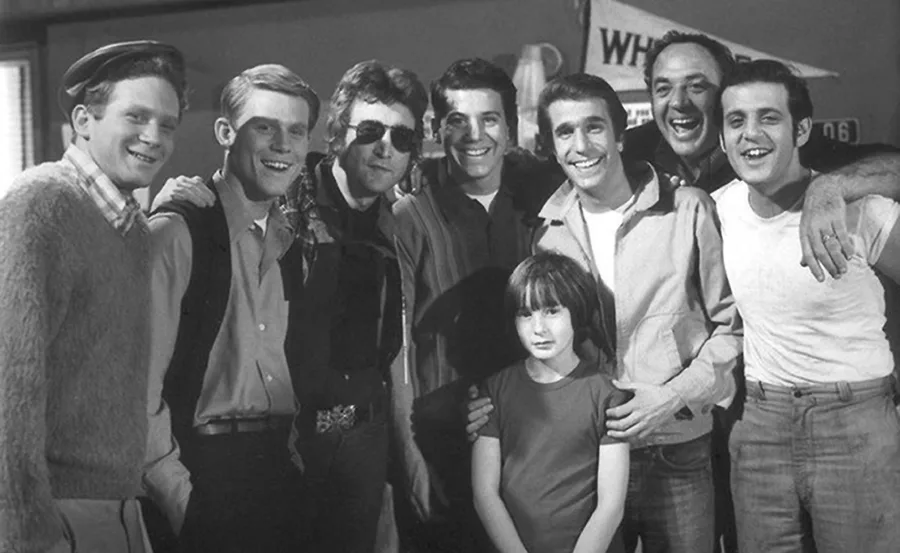 "Black and white photo of the Happy Days cast posing together, smiling, with a young girl in front."