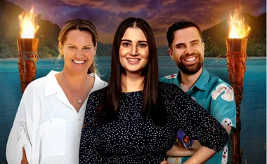Three people smiling with tiki torches aflame in the background on a tropical island setting.