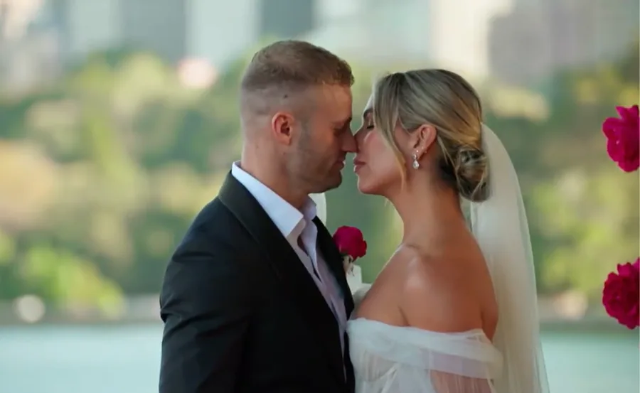 A bride and groom face each other closely, about to kiss, with a blurred nature background.
